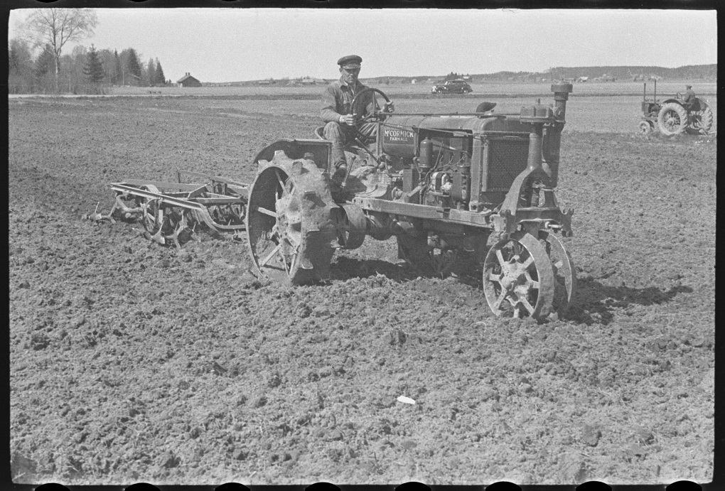 Mustavalkoisessa valokuvassa mies on Farmall F-20 -traktorilla äestämässä peltoa kotimaisella ”Sampo”-traktoriäkeellä.